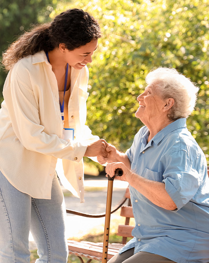 young caregiver assisting elderly woman outdoors with cane in a park promoting companionship and wellness for seniors ideal support for 7 generations